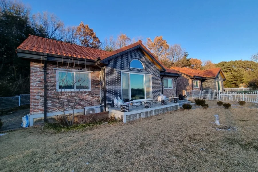 테라코타 기와지붕과 아치형 통유리창이 있는 붉은 벽돌 전원주택 외관
